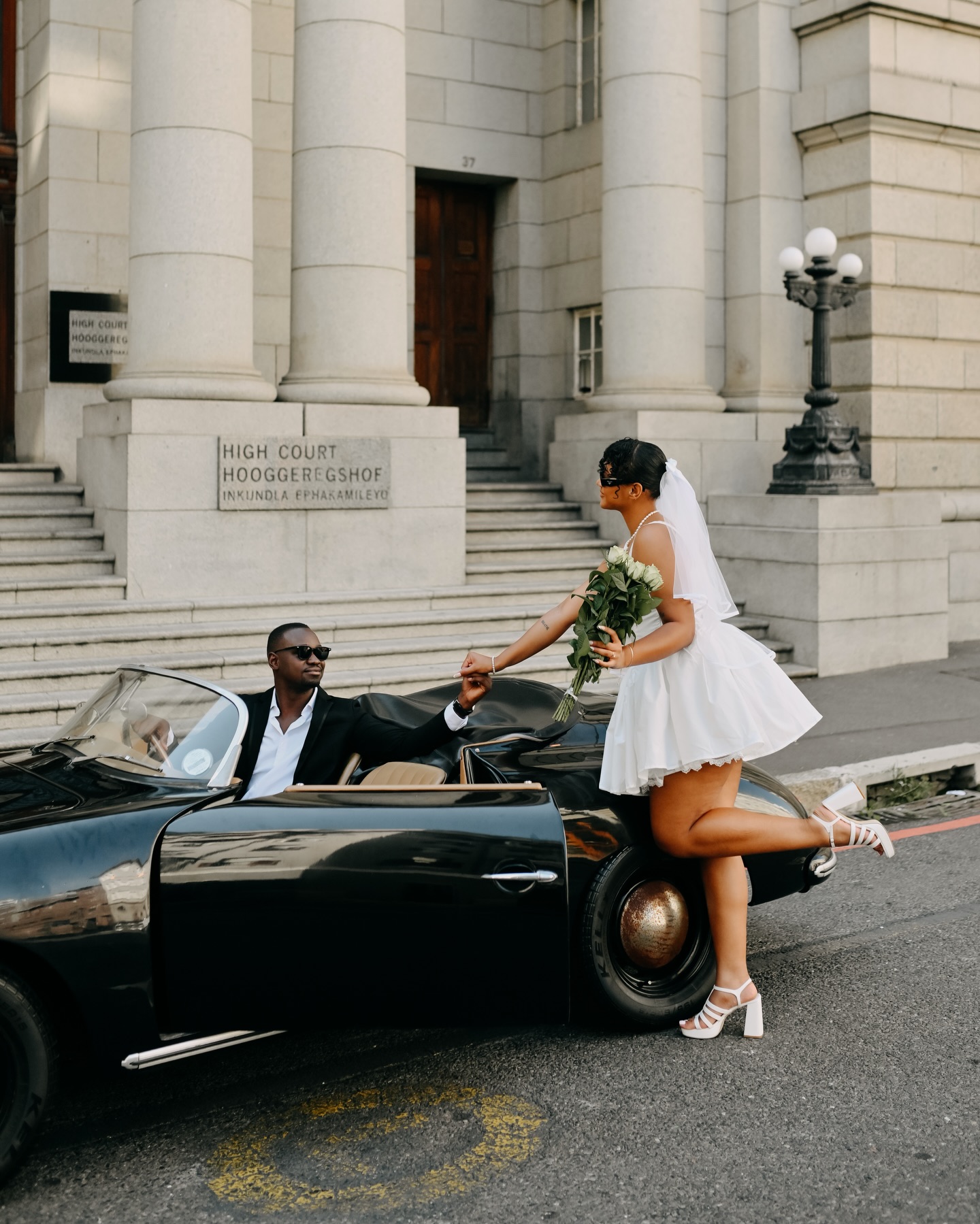 Bride holding the seated groom’s hand beside the open Speedster door